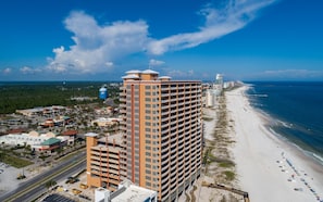 A high-rise hotel with multiple floors, a beach, and a water tower in the background. - Phoenix Orange Beach by Brett/Robinson Vacations (Orange Beach)