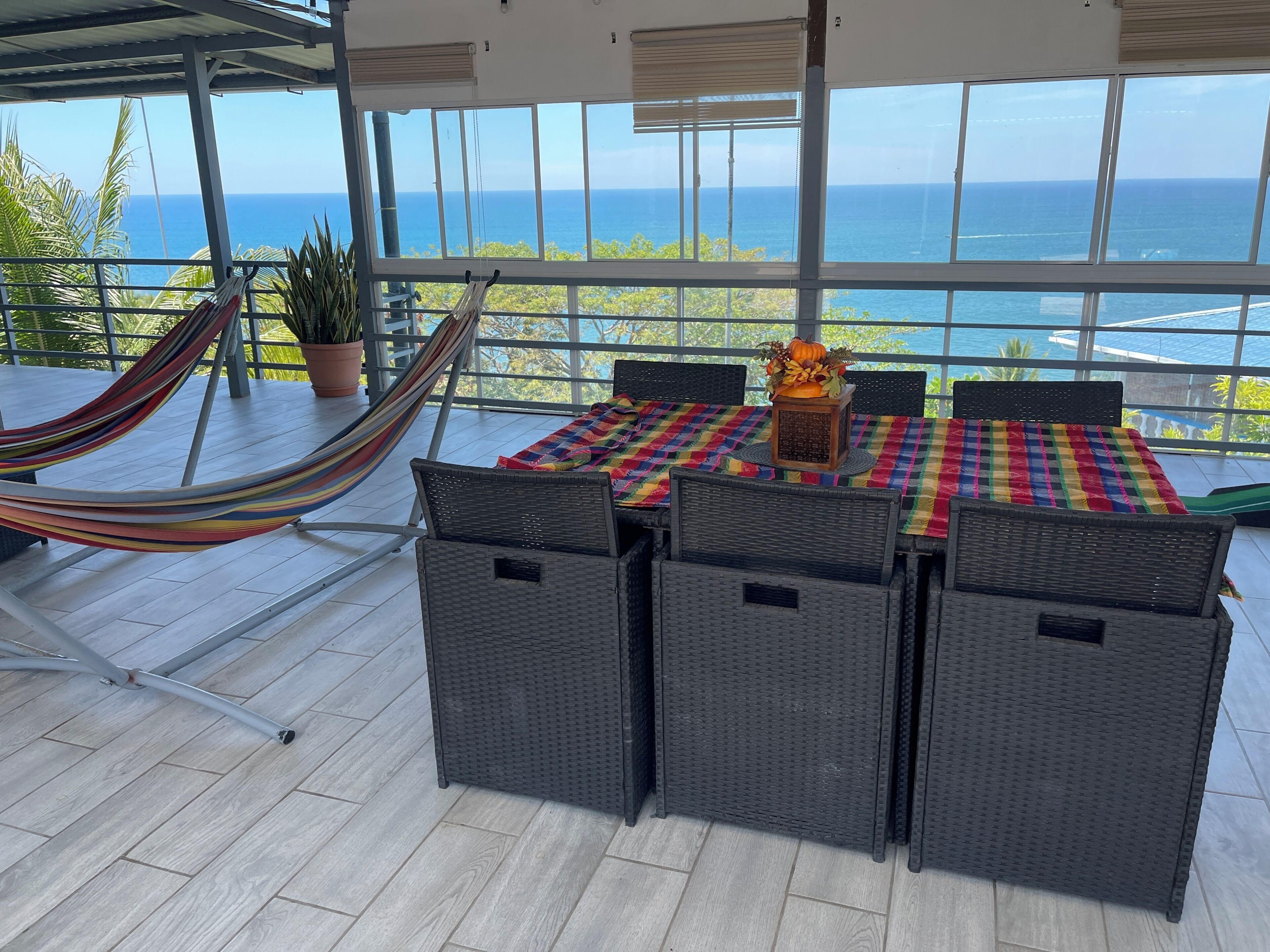 Ein Balkon mit Blick auf das Meer, eine Hängematte, Korbmöbel und ein Tisch mit bunten Tischdecken.