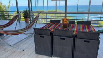 Ein Balkon mit Blick auf das Meer, eine Hängematte, Korbmöbel und ein Tisch mit bunten Tischdecken.