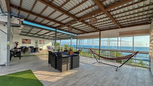 A spacious indoor area with a high ceiling, a seating area with a table, and a hammock. - Solarium Beach House in Atami with ocean View (Tamanique)