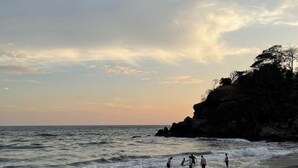 A beach with waves, a rocky outcrop, and a few people in the water. - Solarium Beach House in Atami with ocean View (Tamanique)