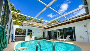 A swimming pool with a glass ceiling, surrounded by lounge chairs and a view of palm trees. - Singer Island pool home (West Palm Beach)