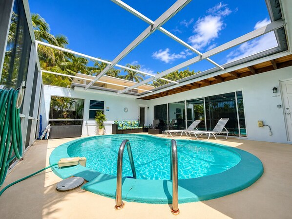 A swimming pool with a glass ceiling, surrounded by lounge chairs and a view of palm trees.