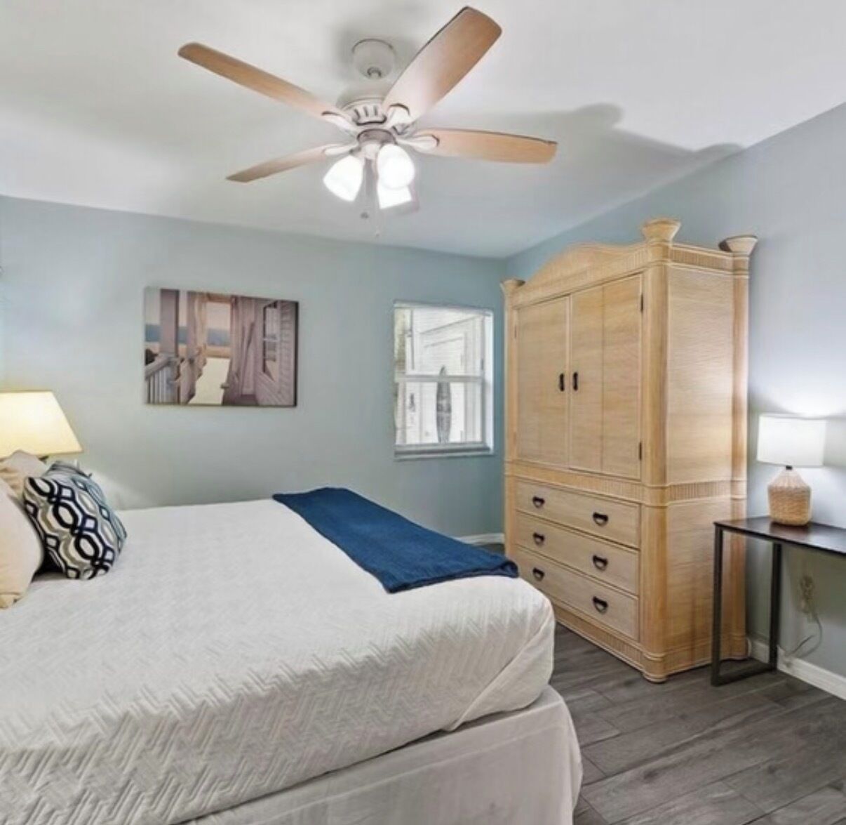 Une chambre à coucher avec un lit, une armoire, un ventilateur de plafond, une fenêtre et une lampe.