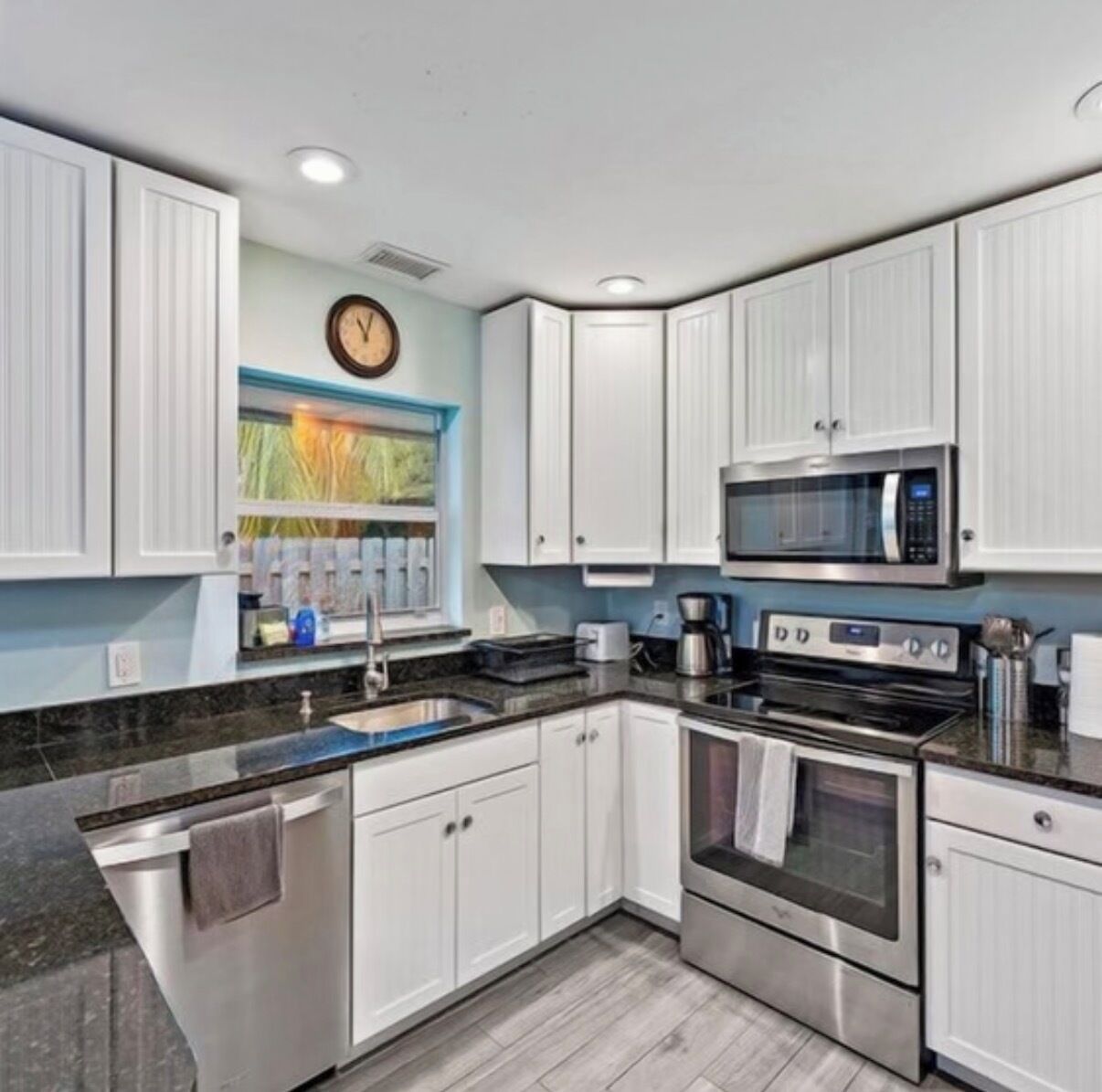 Une cuisine moderne avec des meubles blancs, un four en acier inoxydable, un four à micro-ondes et une fenêtre donnant sur un paysage verdoyant.