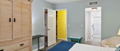 Une chambre à coucher comprenant un lit, une armoire, un ventilateur de plafond et une porte donnant sur une autre pièce.