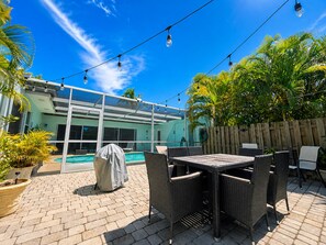 An outdoor patio with a pool, covered seating, and string lights.