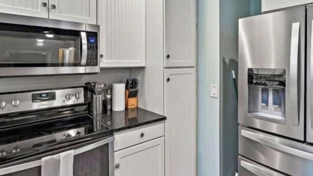 A kitchen with white cabinetry, a microwave, a stove, and a refrigerator. - Singer Island pool home (West Palm Beach)
