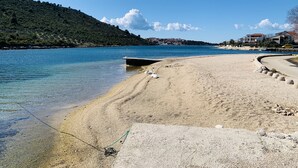 Uma praia com águas cristalinas, uma estrutura de concreto e edifícios ao fundo.