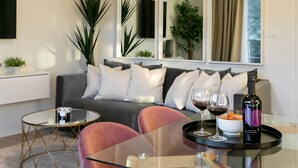 Uma sala de estar moderna com um sofá cinzento, uma mesa de centro de vidro e uma garrafa de vinho sobre um porta-bandeja.