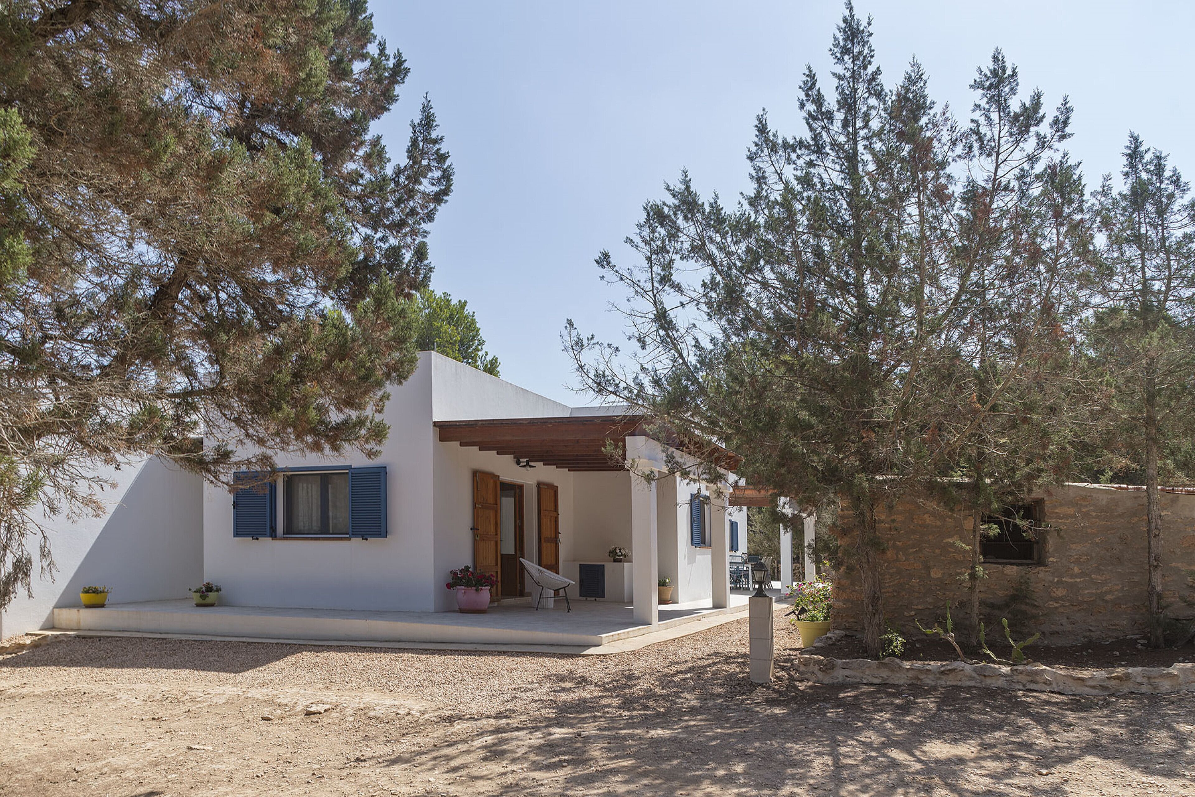 A modern house with a covered porch, a small garden, and a rustic building in the background.