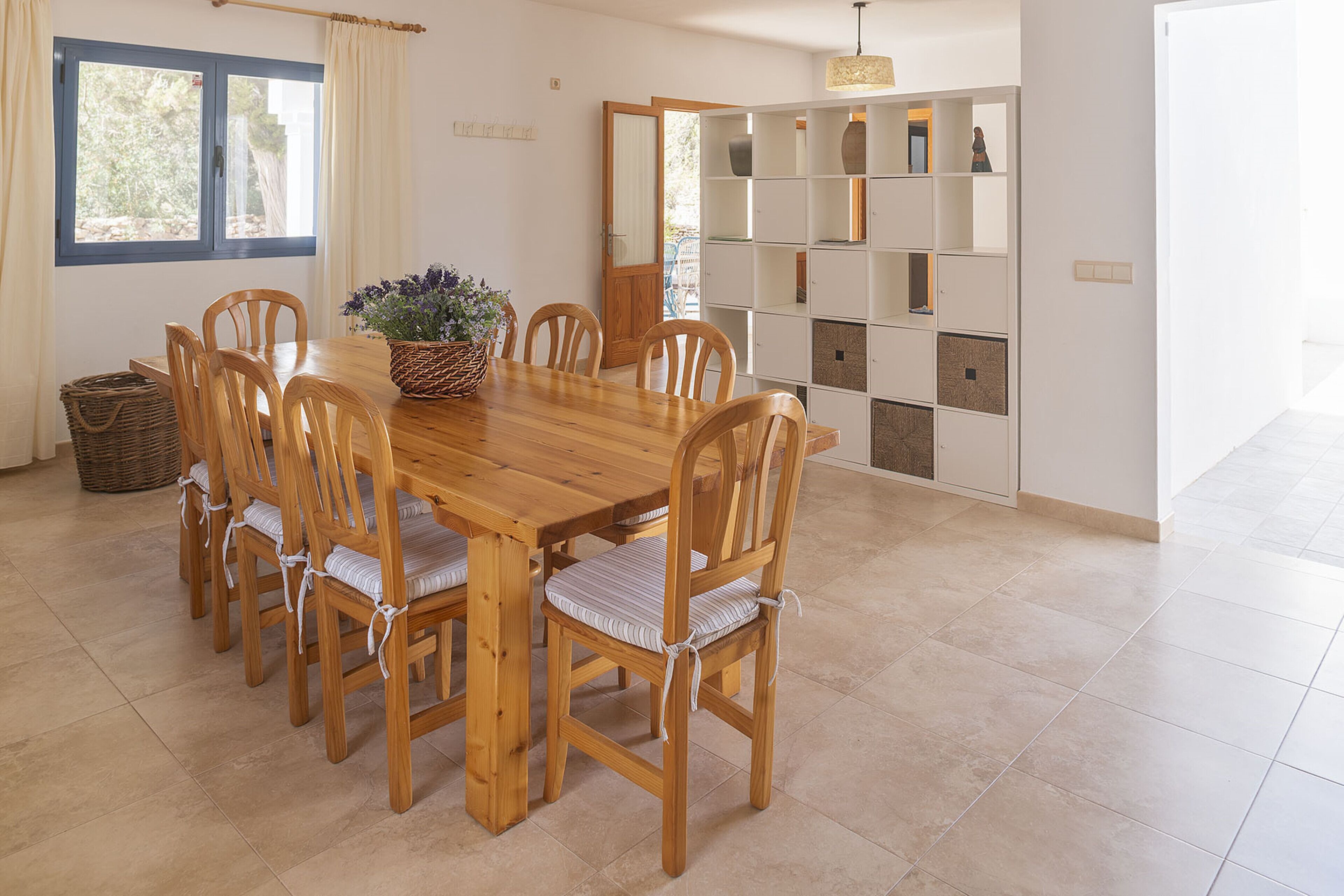 Ein Essbereich mit Holztisch und -stühlen, einem Blumenkorb und einer weißen Regaleinrichtung an der Wand.