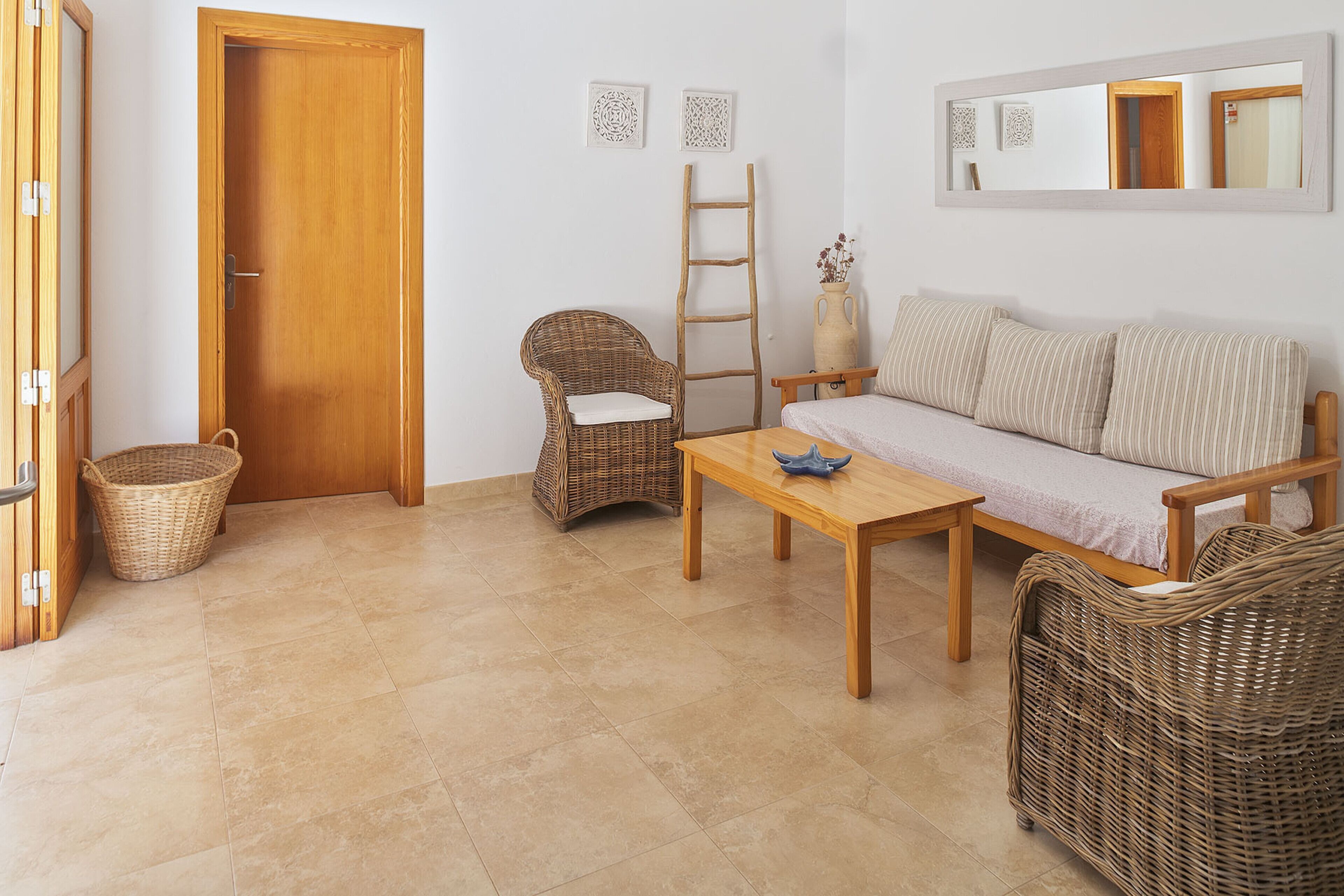 A room with a wooden door, wicker furniture, a wooden table, a sofa, a wicker chair, a small wicker basket, and a wooden ladder.