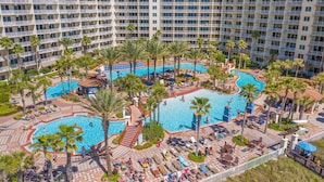Un hotel grande con múltiples balcones, una piscina central y palmeras a su alrededor.