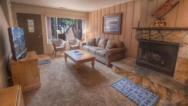 A cozy living room with a stone fireplace, a sofa, a coffee table, and wicker chairs. - Heavenly Mountain Hideaway 2 Bedroom Home by RedAwning (South Lake Tahoe)