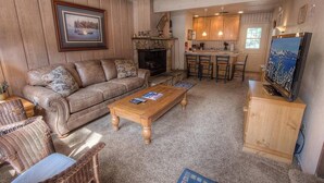A cozy living room with a sofa, coffee table, and wicker chairs. A fireplace and kitchen area with bar stools are visible in the background. - Heavenly Mountain Hideaway 2 Bedroom Home by RedAwning (South Lake Tahoe)