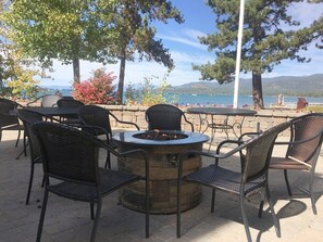 An outdoor seating area with a circular fire pit table surrounded by wicker chairs, overlooking a body of water and mountains. - Bear Lake Hideaway 3 Bedroom Condo by RedAwning (South Lake Tahoe)