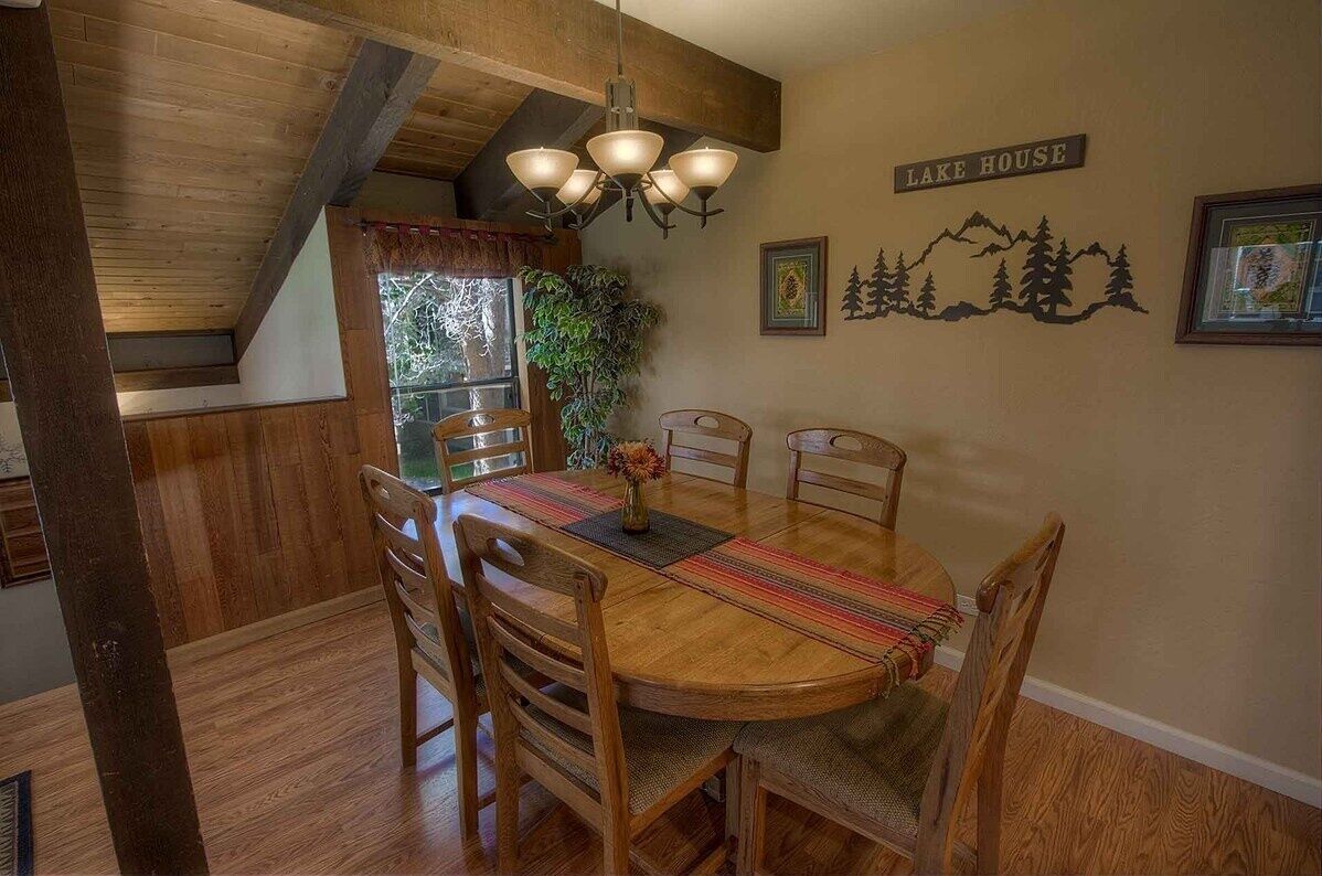 A wooden dining table with six chairs, a chandelier, and a 'Lake House' sign on the wall.