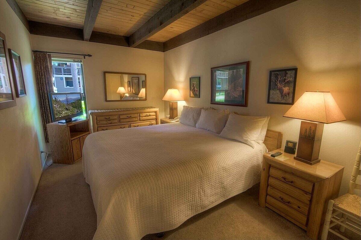 A cozy bedroom with a large bed, wooden headboard, bedside tables with lamps, and framed pictures on the walls.