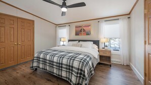 Une chambre à coucher comprenant un lit, des tables de chevet, un ventilateur de plafond et une armoire en bois.