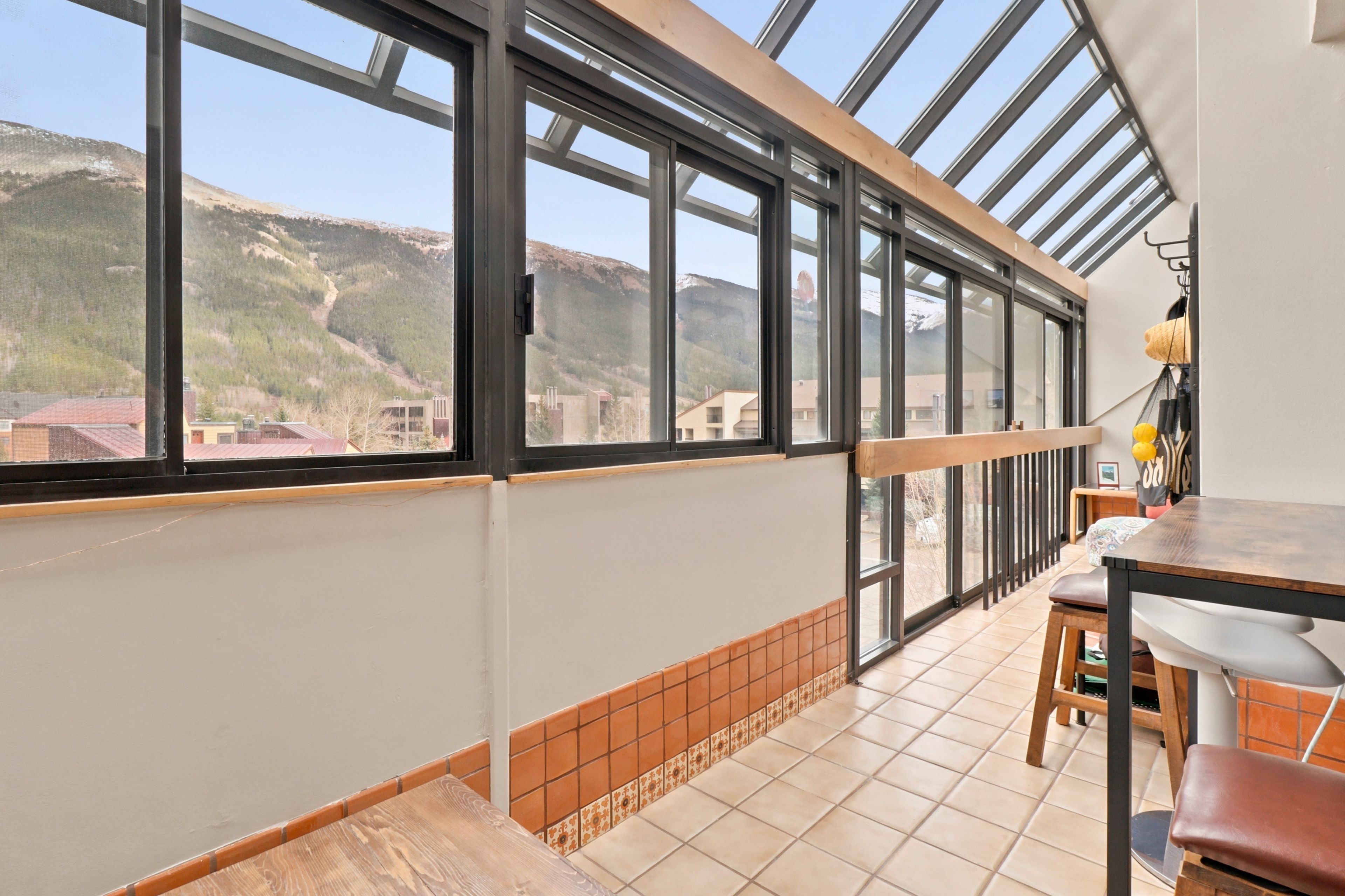 A room with a large window overlooking a mountainous landscape, a wooden table, and a chair.