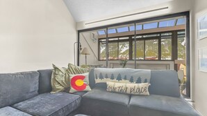 A modern living room with a grey sectional sofa, a small wooden table, and a large window offering a view of a snowy mountain. - Wh405 Wheeler House 3 Bedroom Condo by RedAwning (Copper Mountain)