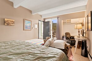 Habitación de hotel con una cama, un escritorio con computadora, una silla y una ventana con cortinas.