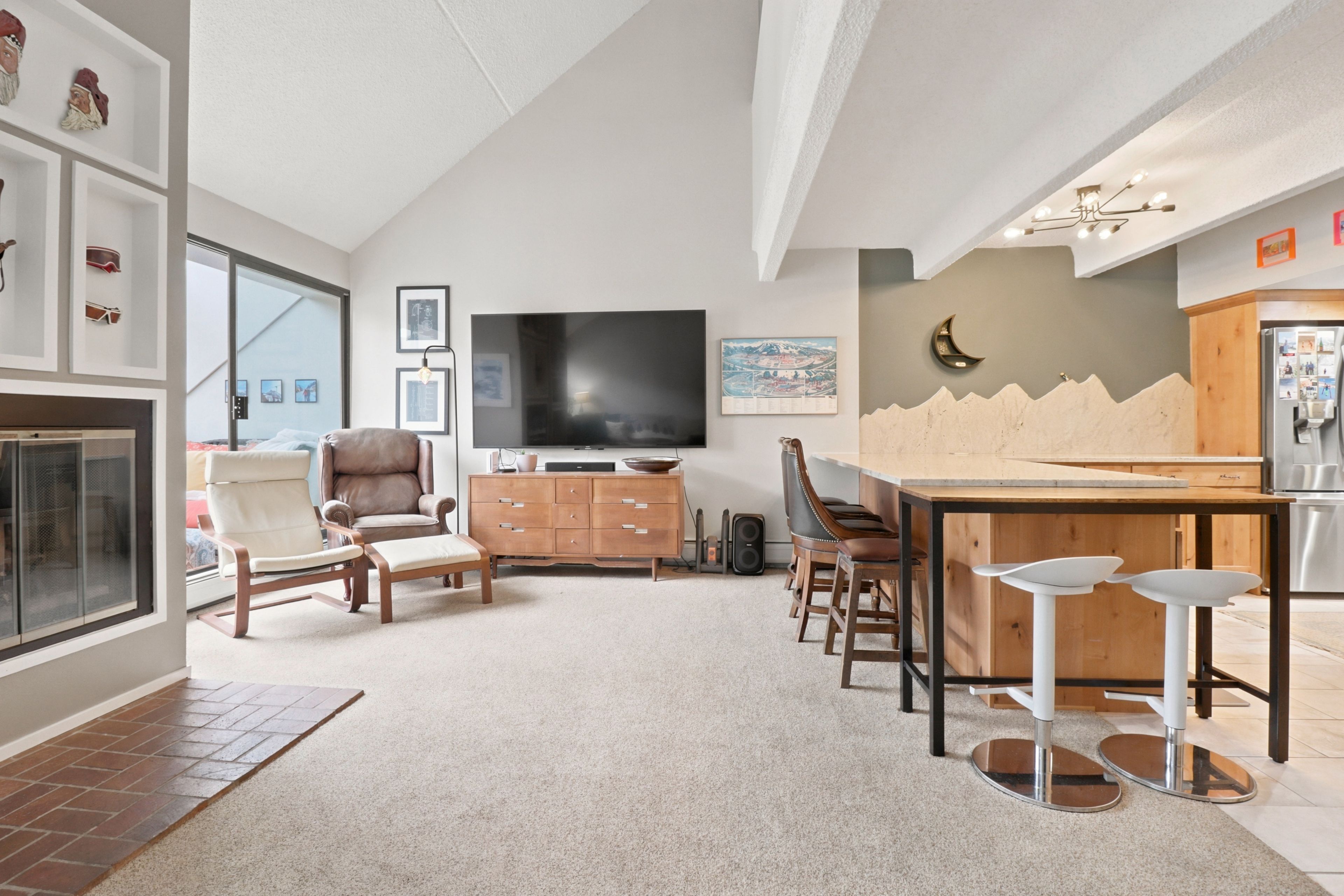 A modern living room with a fireplace, seating area, and a kitchen with a dining table.
