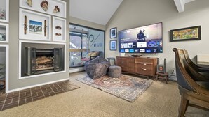 A living room with a fireplace, a large flat-screen TV, and a view of the outdoors through a sliding door. - Wh405 Wheeler House 3 Bedroom Condo by RedAwning (Copper Mountain)