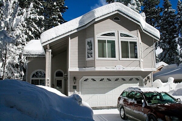 Una casa de dos pisos con garaje, rodeada de árboles cubiertos de nieve.