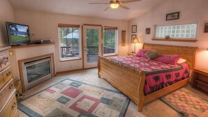 A bedroom with a wooden bed, a television, a ceiling fan, and large windows. - Wolfpack Refuge 4 Bedroom Home by RedAwning (South Lake Tahoe)