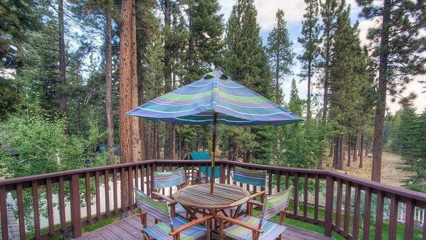 A wooden deck with a table and chairs, surrounded by a wooden railing, set in a forested area. - Wolfpack Refuge 4 Bedroom Home by RedAwning (South Lake Tahoe)