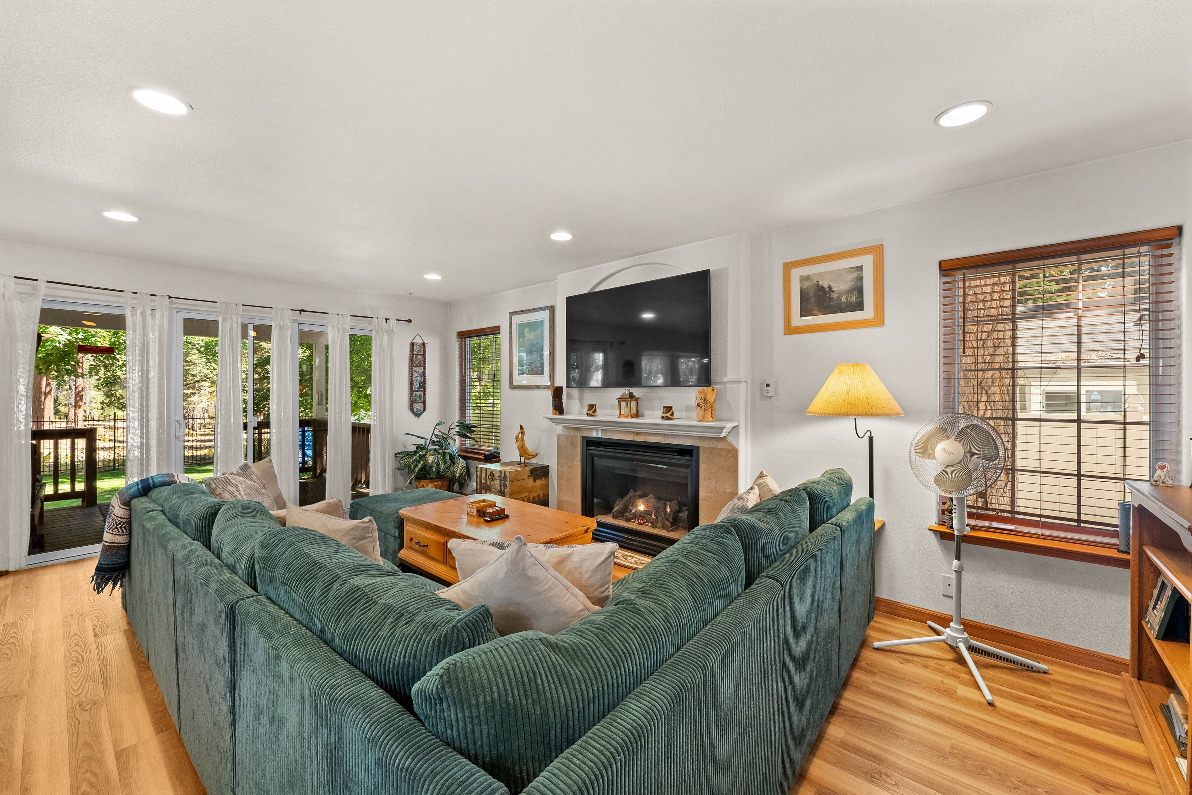 A modern living room with a sectional sofa, a fireplace, a television, and a large window with blinds.