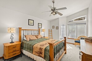 Een slaapkamer met een bed, nachtkastjes, een bureau, een stoel, een plafondventilator en een raam met jaloezieën.