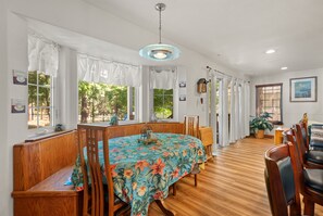 Uma sala de jantar com mesa redonda coberta por toalha florida, cadeiras de madeira e luminária pendente.