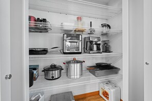 Cozinha com prateleiras brancas, cafeteira, chaleira, torradeira, panela e uma caixa de leite.
