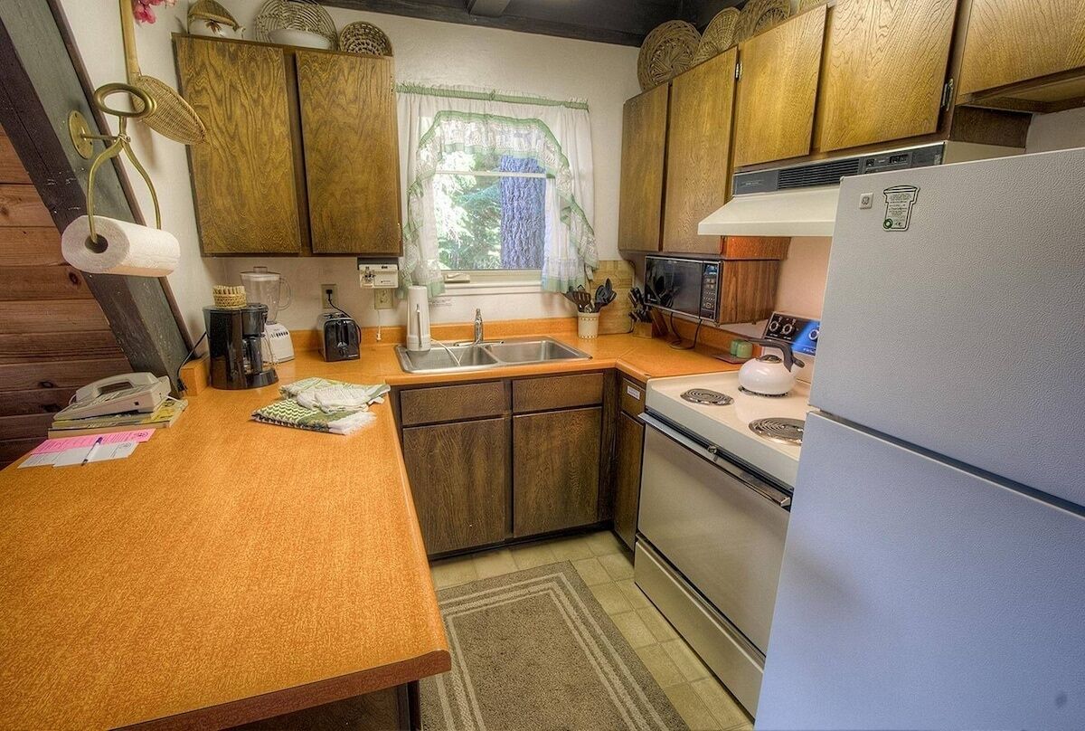 A compact kitchen with wooden cabinets, a stainless steel refrigerator, a sink, and a microwave.