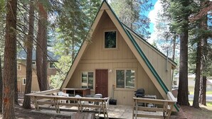 A cabin with a triangular roof, a front door, and a small porch with benches. - Lodgepole Chalet 3 Bedroom Home by RedAwning (South Lake Tahoe)