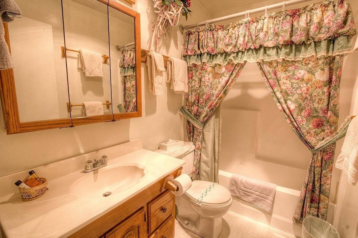 A bathroom with a wooden vanity, a large mirror, a toilet, and a shower area with floral curtains.