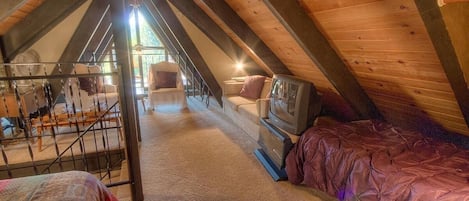 Une chambre confortable située dans les combles, avec un plafond en pente, un lit, une télévision et un escalier menant à une autre pièce.