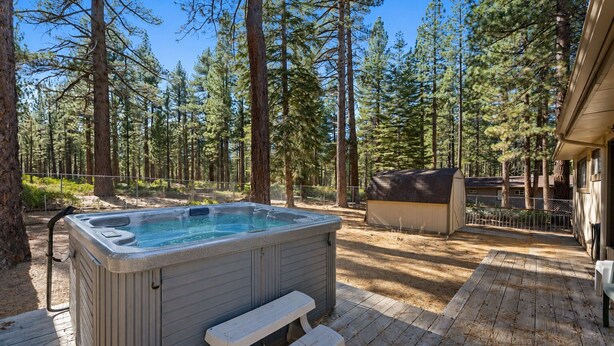 Een hottub op een houten terras met een bank, omringd door een bos.