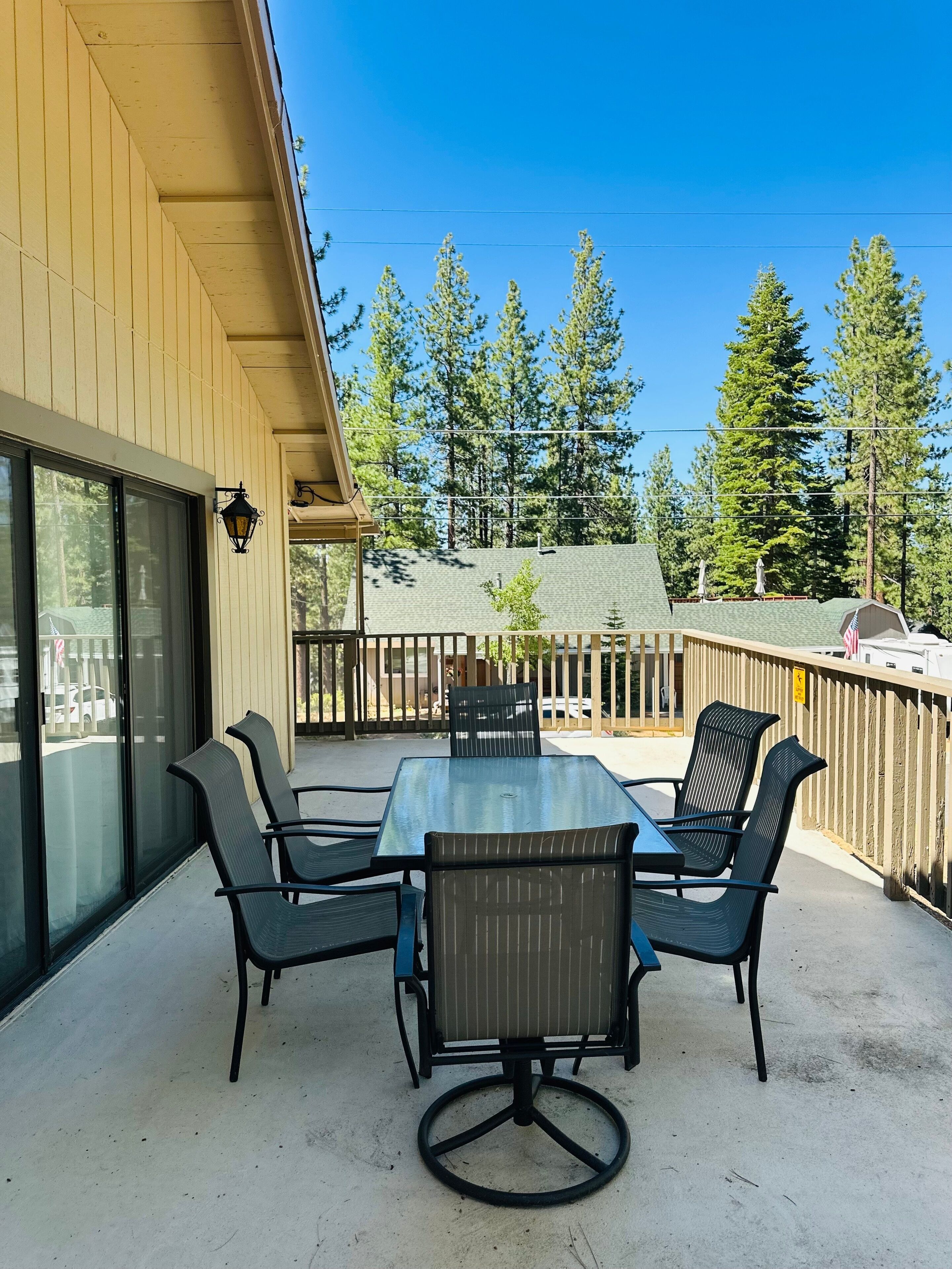A covered patio with a table and chairs, a wooden fence, and a view of trees and a building in the background.