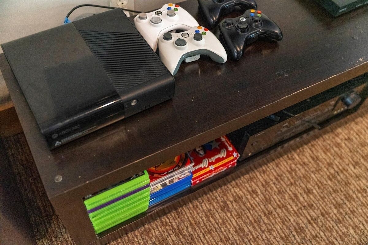 A wooden table with two Xbox controllers and a black gaming console.
