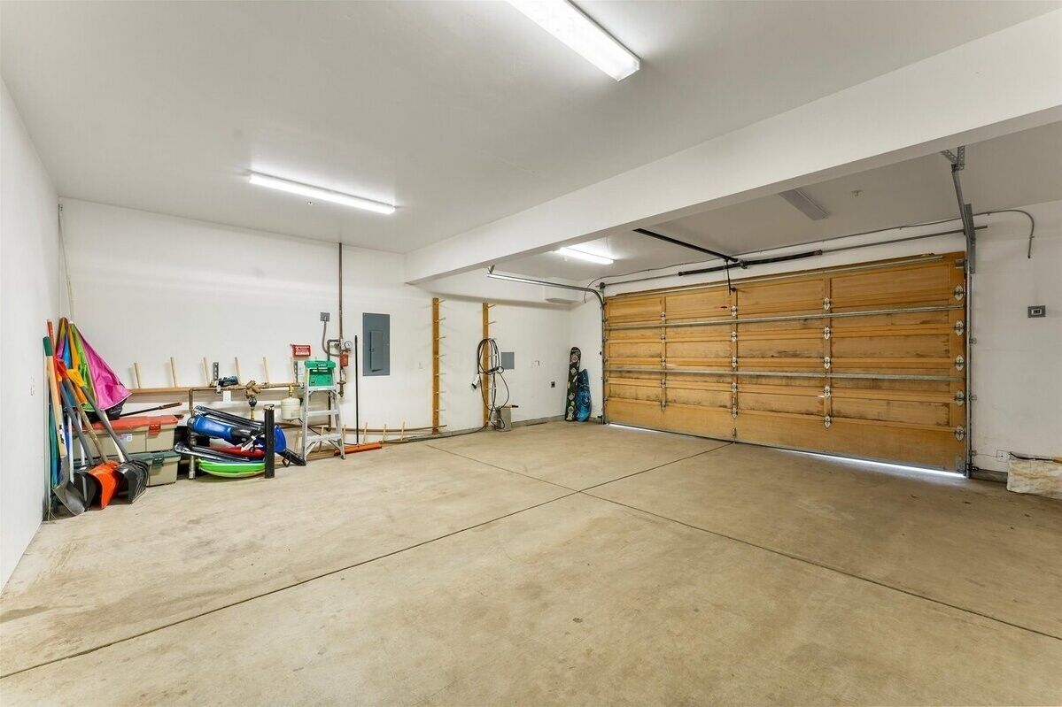 A spacious garage with a large wooden garage door, concrete floor, and overhead fluorescent lighting.