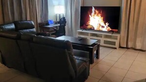 A living room with a leather sofa, a TV displaying a fire, and a white entertainment unit.