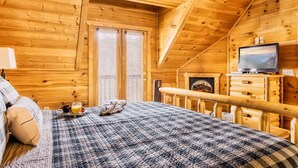 Un dormitorio de cabaña de madera con cama, televisor y chimenea.
