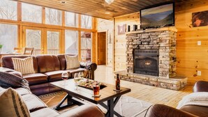 Una sala de estar acogedora con chimenea de piedra, sofá de cuero y televisor montado en la pared.