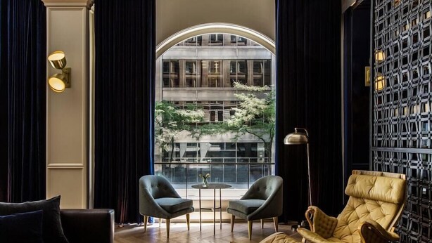 A modern interior with a sofa, two armchairs, a round table, and a decorative chair. A large window offers a view of a building and trees outside. - 1-Bedroom Suite at a 4.5⭐️ Hotel (Chicago)
