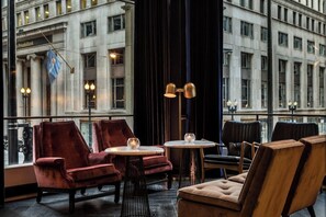 A room with a large window, a red velvet armchair, a round table with a glass object, and a lamp. - 1-Bedroom Suite at a 4.5⭐️ Hotel (Chicago)