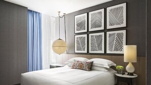 A modern hotel room with a large bed, a bedside table with a lamp, and a wall with geometric patterned artwork. - 1-Bedroom Suite at a 4.5⭐️ Hotel (Chicago)